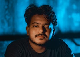 Close-up portrait of a young man with a thoughtful expression against a blue backdrop.